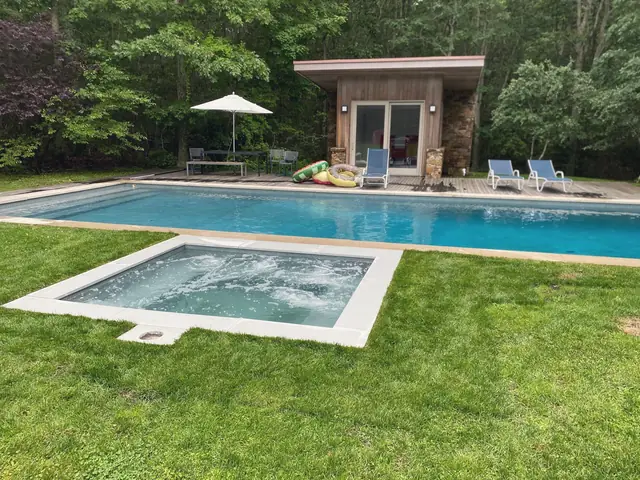 Pool and square spa beside a lawn and cedar pool house