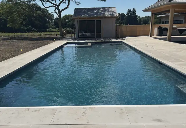 Newly finished pool with stone coping beside a pool house